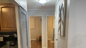 Un couloir avec un plancher en bois, un coin cuisine doté de plans de travail en granit et une œuvre d’art encadrée accrochée au mur.