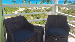 A balcony with wicker chairs overlooking a beach with clear blue water and palm trees. - Colorful Beach Home w/ Ocean Front View + 2 Master Bedrooms (Exuma)