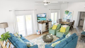 A spacious living room with blue sofas, a coffee table, and a TV on a wooden stand. - Colorful Beach Home w/ Ocean Front View + 2 Master Bedrooms (Exuma)
