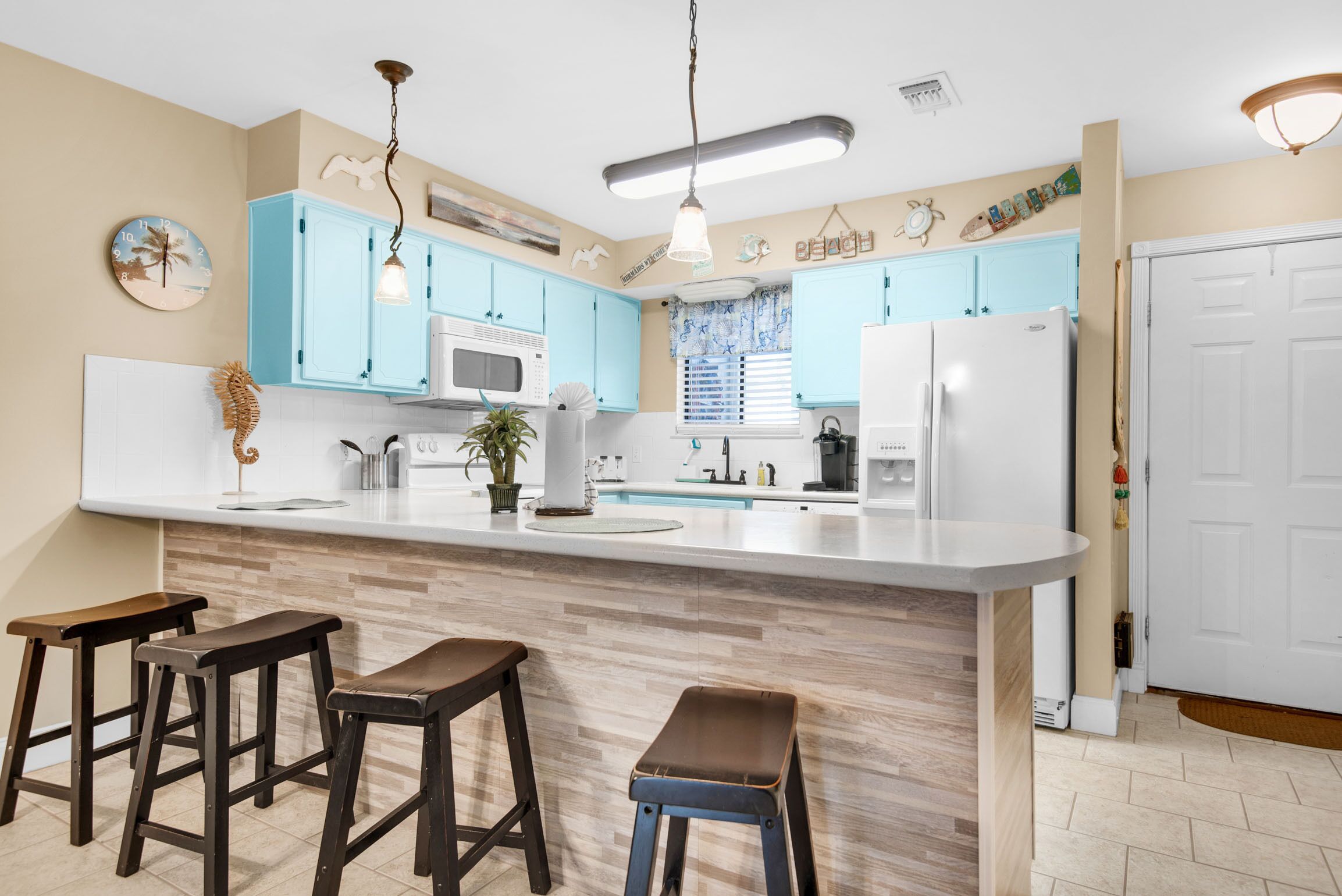 Une cuisine avec des meubles de couleur bleu clair, un réfrigérateur blanc et un îlot central en bois doté de tabourets.