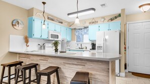A kitchen with light blue cabinets, a white refrigerator, and a wooden island with stools.