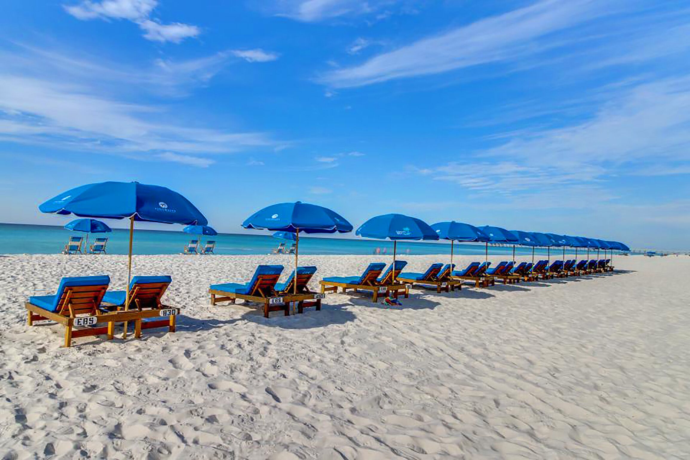 A beach with rows of blue umbrellas and wooden lounge chairs.