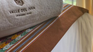 Une serviette roulée ornée du texte « Valle del Inka », posée sur un lit recouvert d’une couverture à rayures colorées.