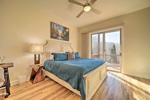 A bedroom with a bed, a nightstand, a lamp, a ceiling fan, and a large window with a view of trees. - Beautiful Whittier Condo w/ Deck + Mtn Views! (Whittier)