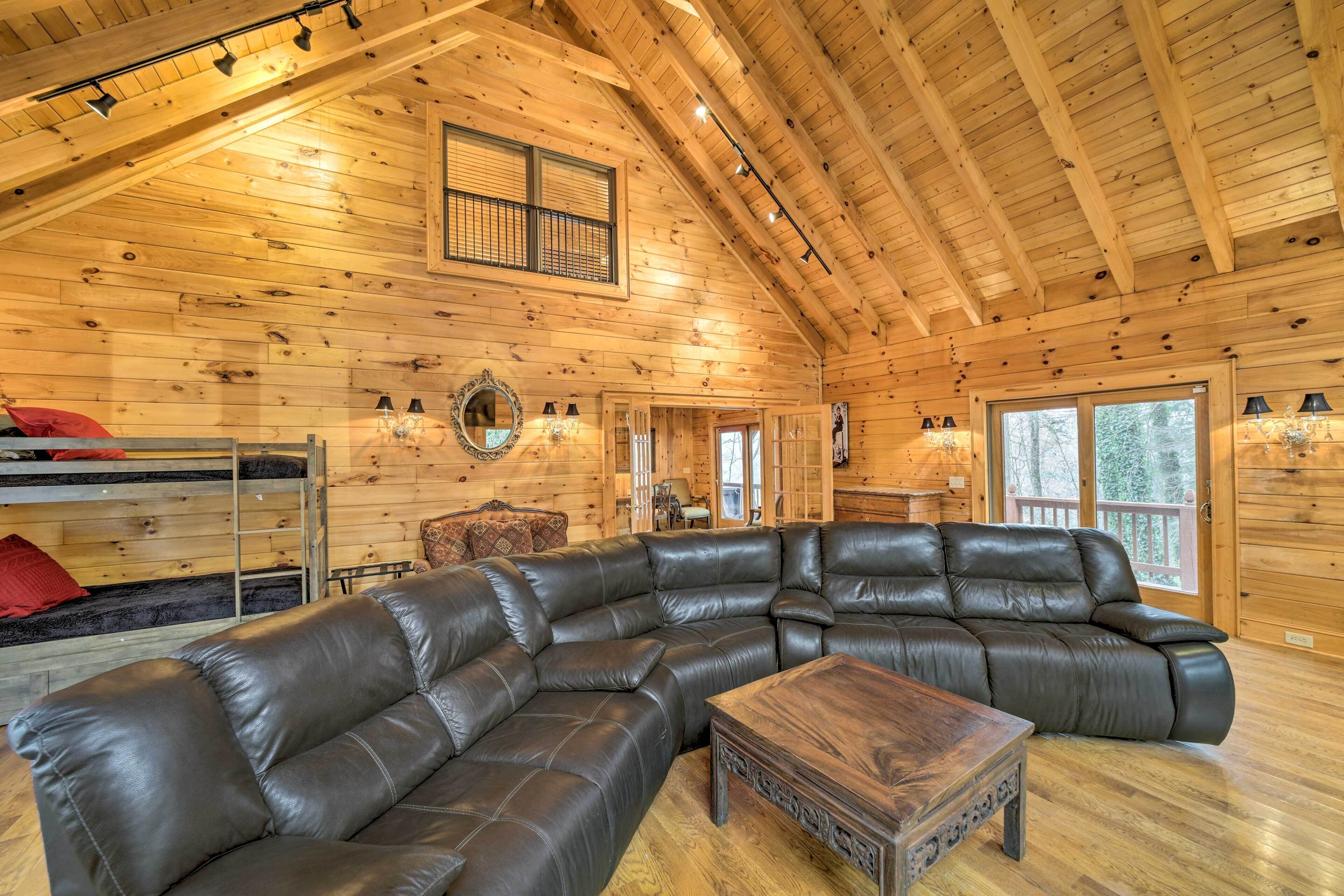 A log cabin interior with a large leather sectional sofa, a wooden coffee table, and a bunk bed with red pillows.