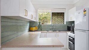 Una cocina moderna con armarios blancos, encimera de granito, pileta de acero inoxidable y refrigerador negro.