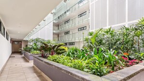 Un couloir intérieur moderne, aménagé en jardin, avec une variété de plantes et une rambarde en verre.