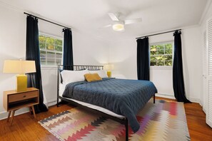 Un dormitorio con una cama, dos lámparas de noche, un ventilador de techo y una ventana con cortinas.