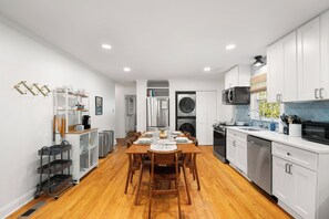 A modern kitchen with white cabinets, a dining area with a wooden table, and a built-in washer and dryer.
