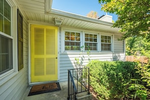 A house with a yellow front door, a small porch, and a well-maintained hedge.