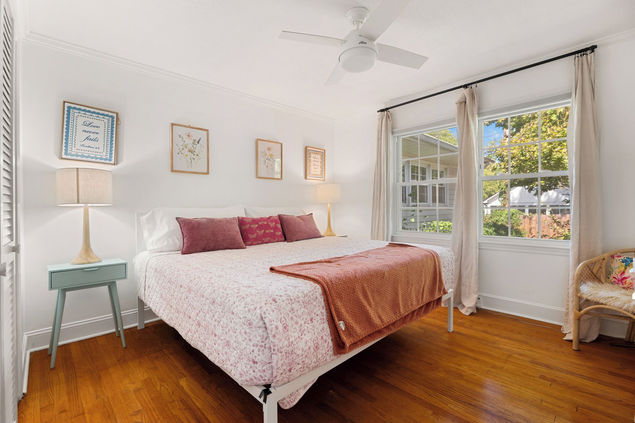 Un dormitorio con cama, lámparas de noche, una ventana con cortinas y un ventilador de techo.