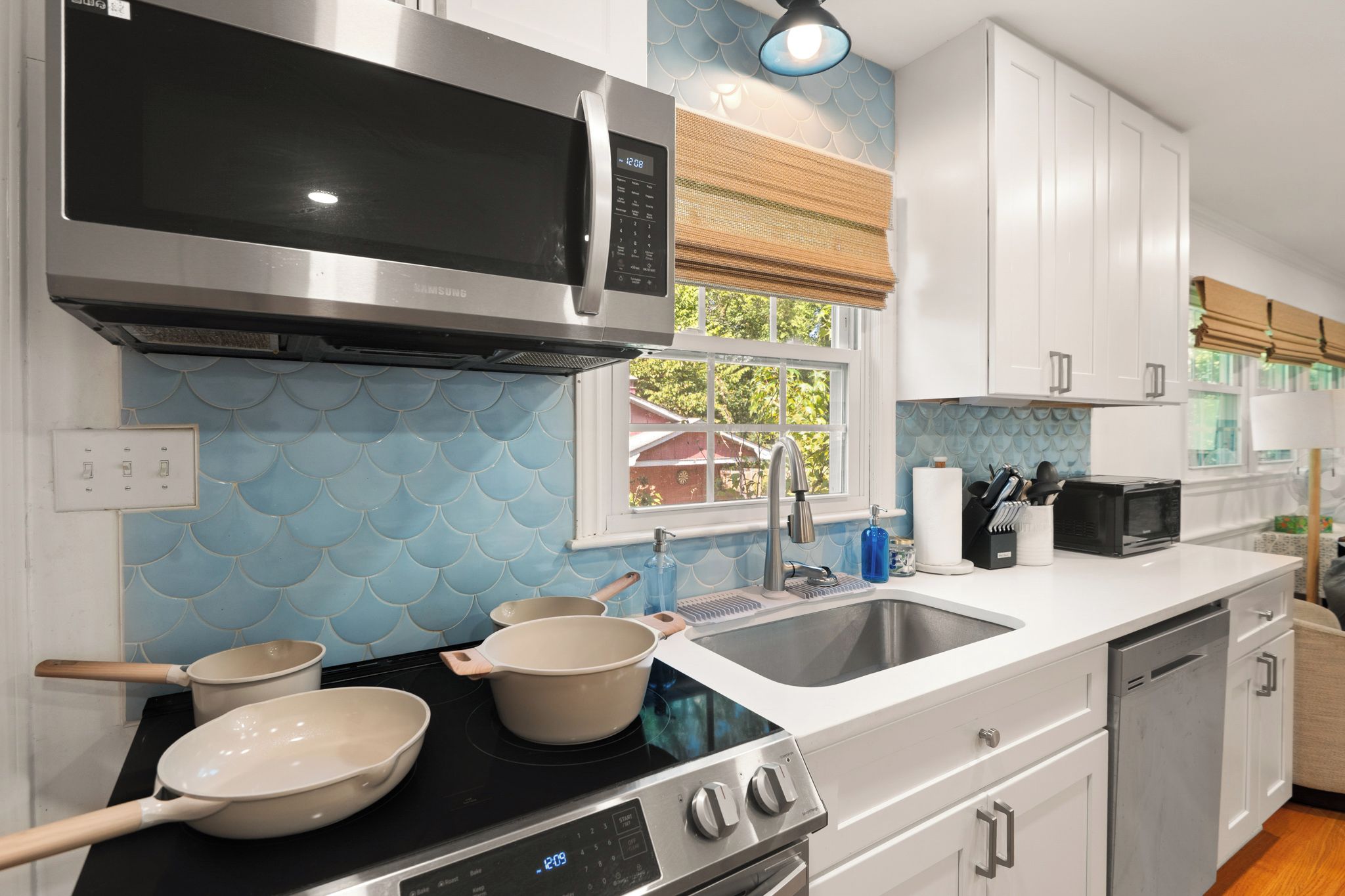 A modern kitchen with stainless steel appliances, a double sink, and a window with a view of a house.