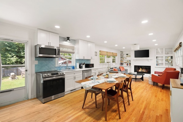 A modern kitchen with a dining area, a fireplace, and a TV mounted on the wall.