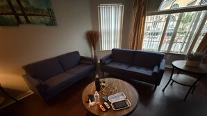 Una sala de estar con sofá, una mesa de centro con dispositivos electrónicos y una ventana con persianas.