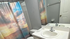 Un baño con lavamanos blanco, inodoro y cortina de ducha con estampado colorido.