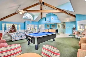 A spacious room with a pool table, a Christmas tree, and a high ceiling with wooden beams.
