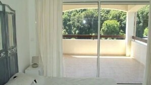 Un dormitorio con un ventanal grande, una cama y vistas a un balcón con árboles.