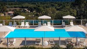 Zona de piscina con sillones y sombrillas, con vistas a un paisaje pintoresco.