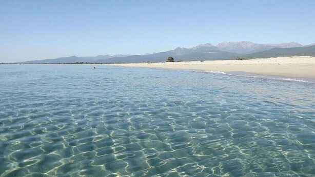 Una playa con agua cristalina, una orilla arenosa y montañas al fondo.