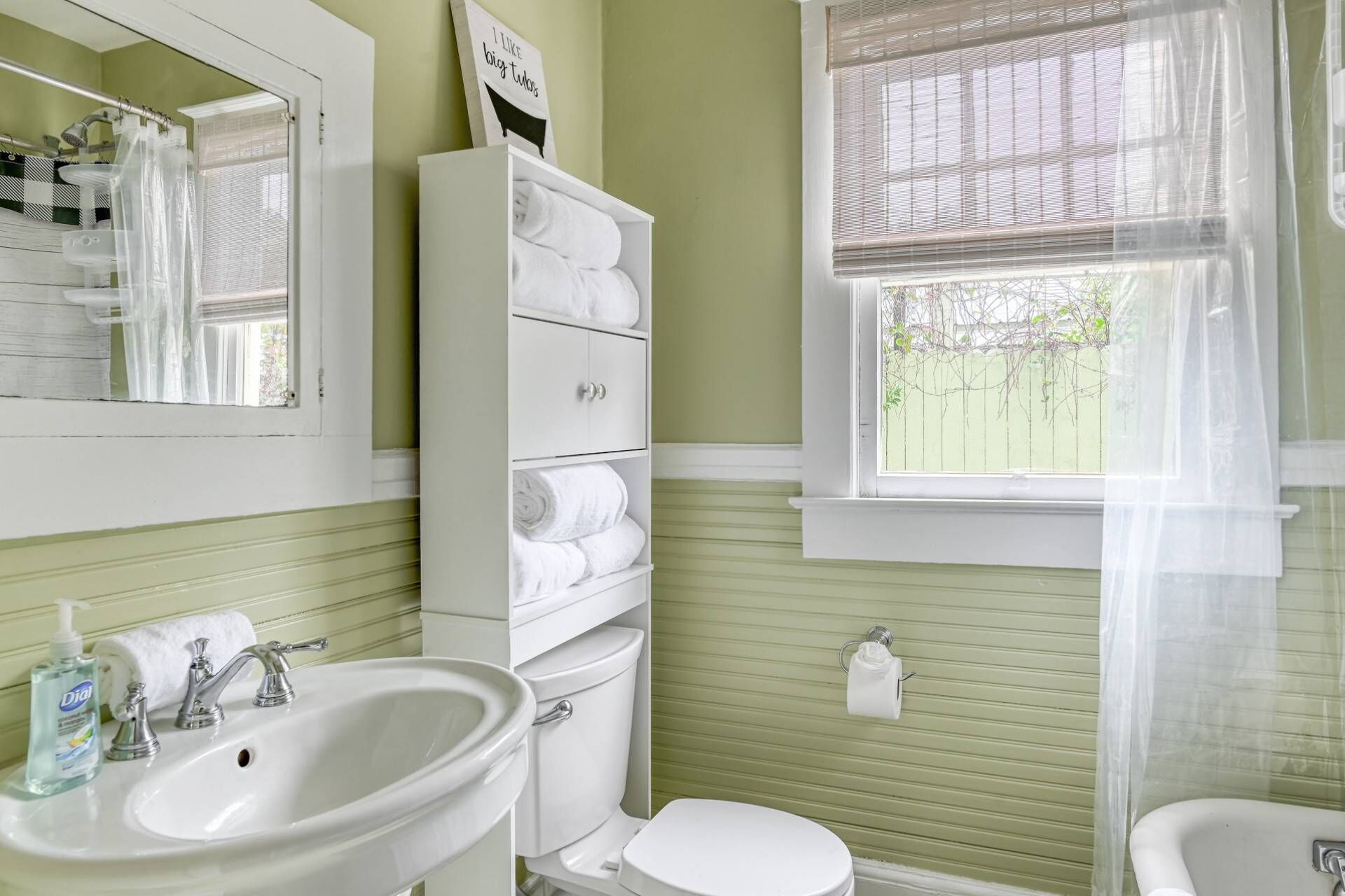 Ein Badezimmer mit Waschbecken, Toilette und einem Fenster mit Blick auf Grünflächen.