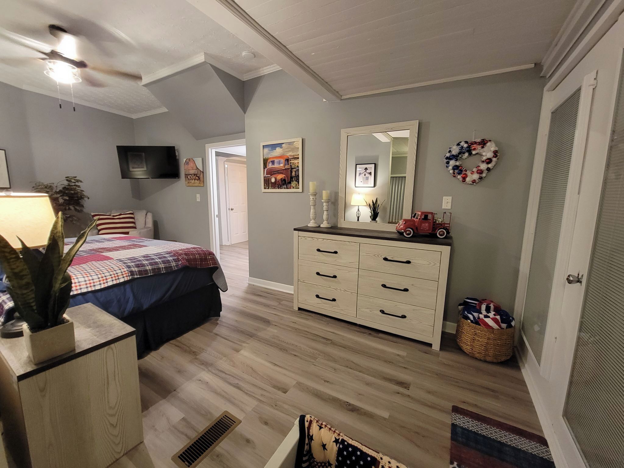 A bedroom with a bed, dresser, mirror, and a television on the wall.