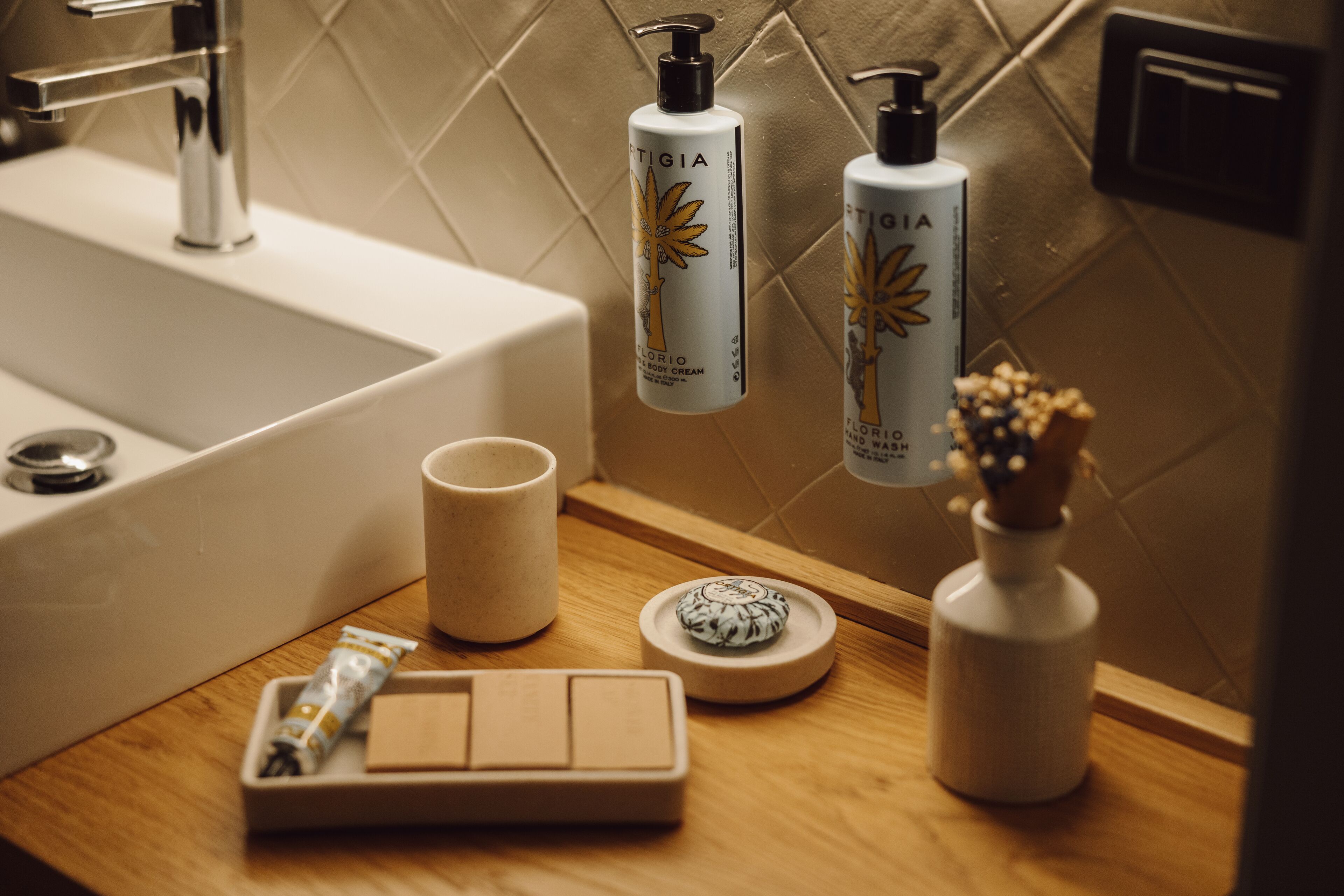 A bathroom with a sink, two bottles of body cream, a cup, and a small decorative item on the counter.