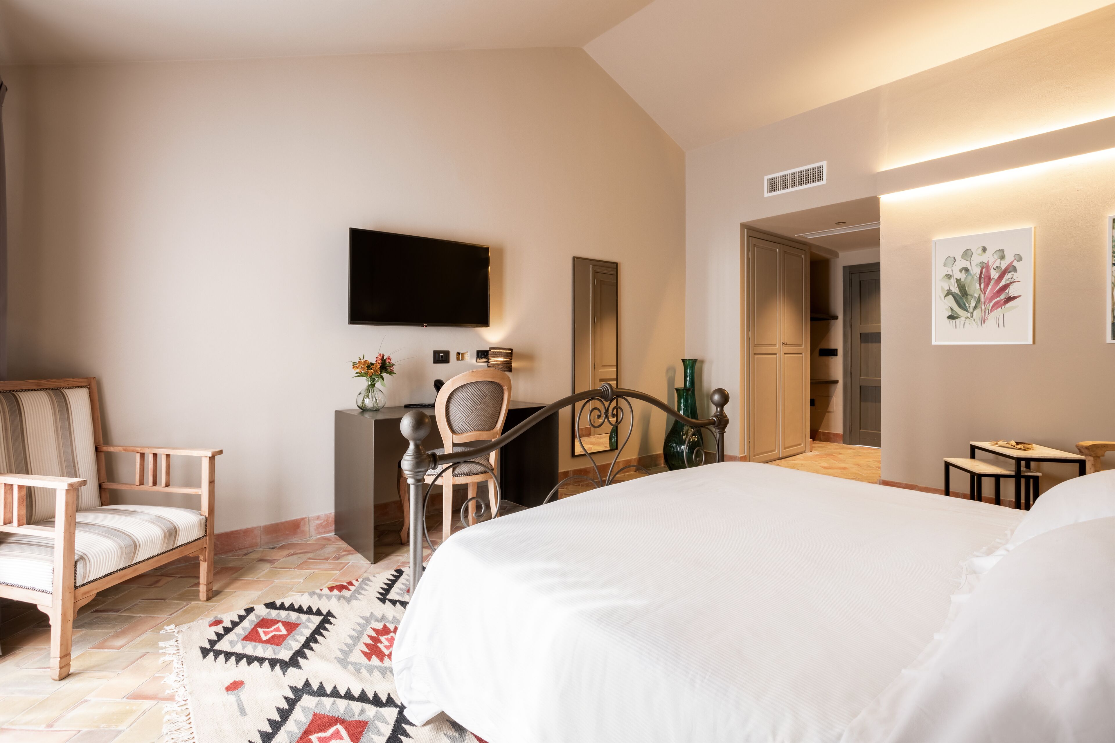 A hotel room with a bed, a desk, a chair, a television, and artwork on the walls.