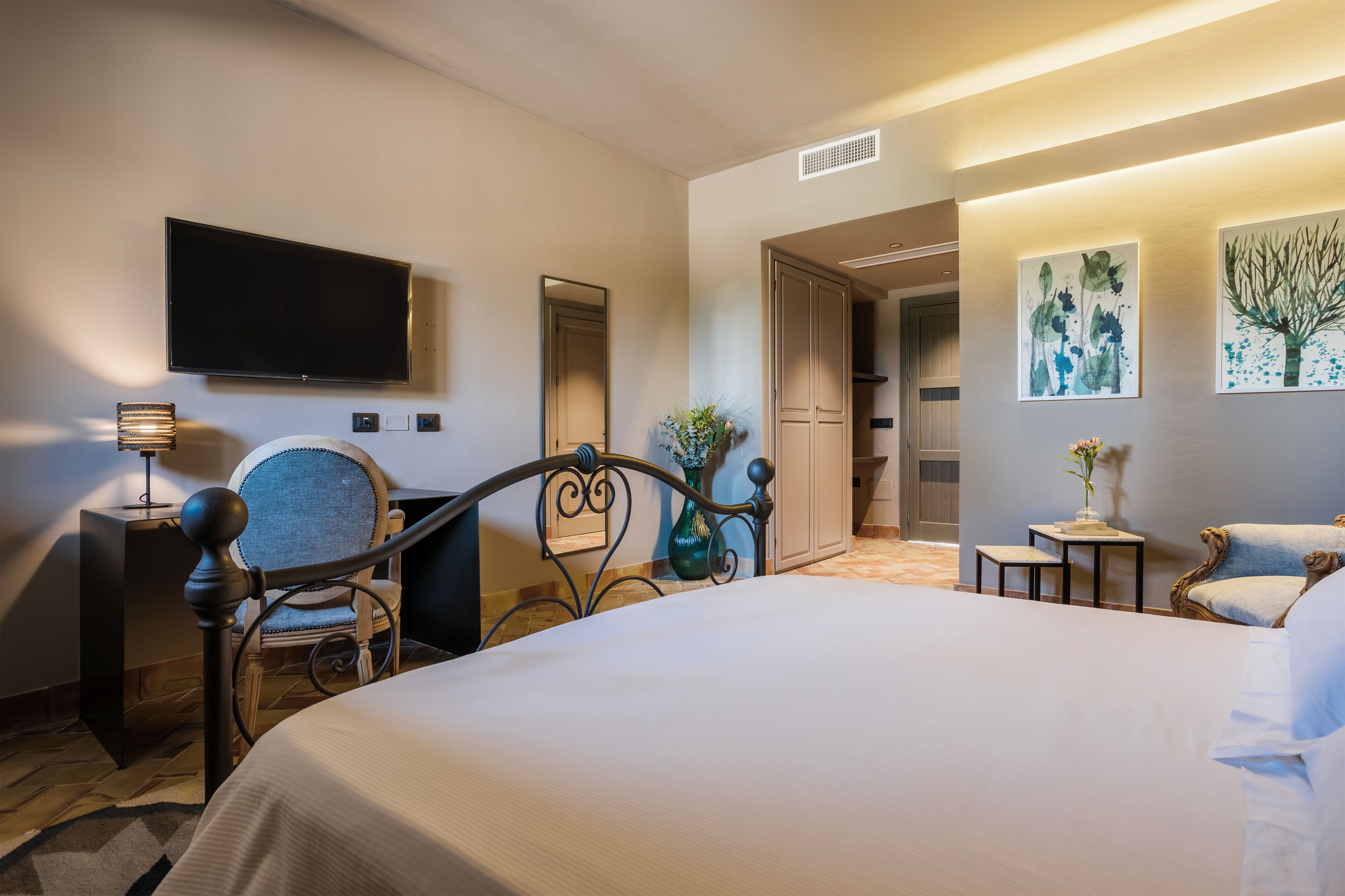 A hotel room with a large bed, a desk, a chair, a television, and artwork on the walls.
