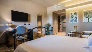 A hotel room with a large bed, a desk, a chair, a television, and artwork on the walls.