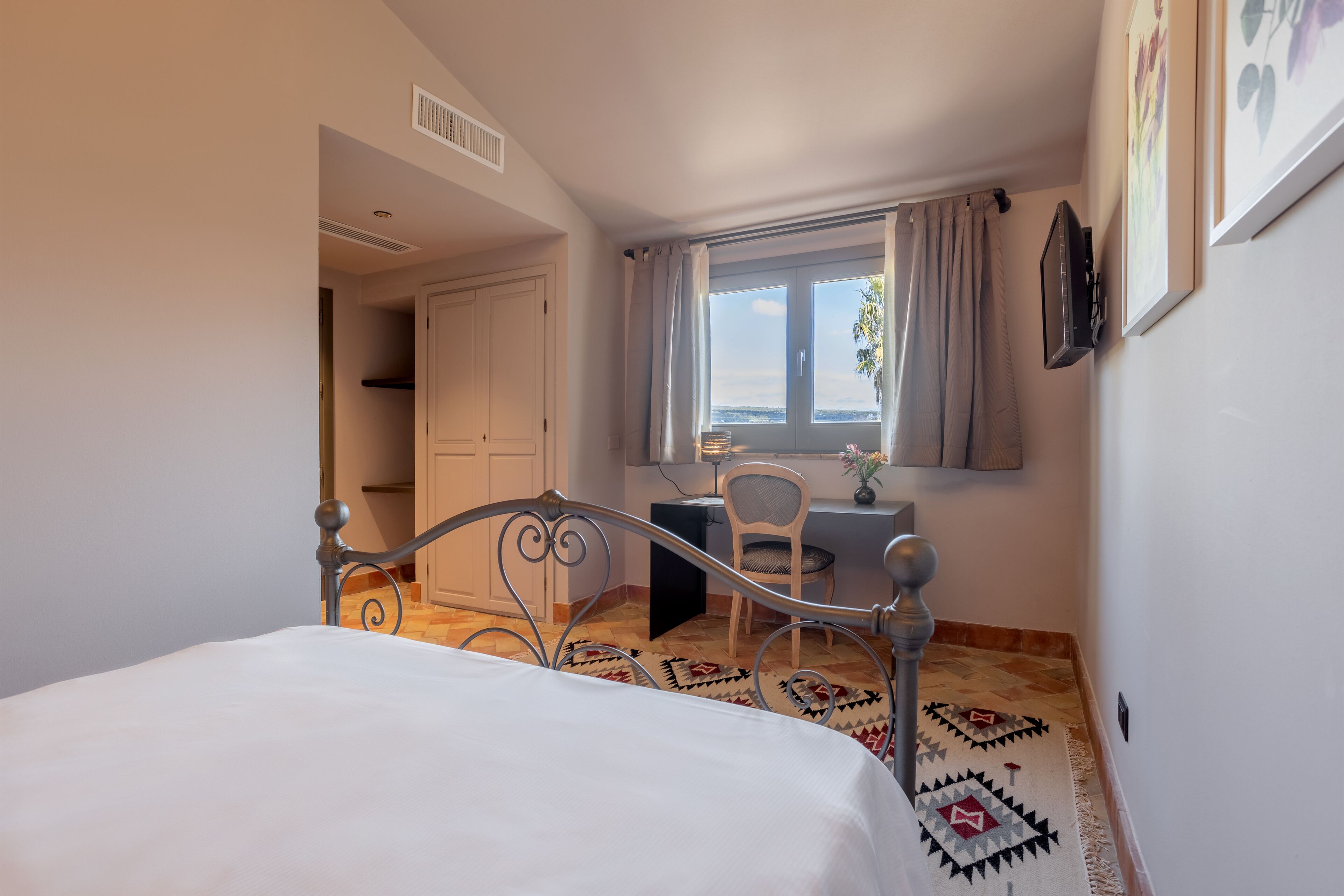 Ein Schlafzimmer mit Bett, Schreibtisch, Stuhl, einem Fenster mit Vorhängen und Meerblick.