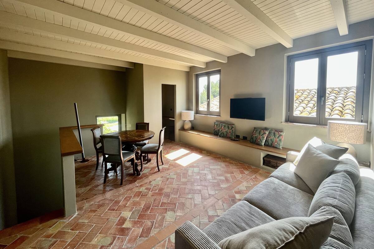 A spacious living area with a dining table, chairs, a sofa, and a TV mounted on the wall.