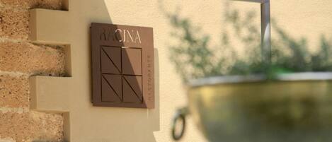 Un letrero sujeto a la pared con el nombre 'RACINA' y un diseño geométrico.