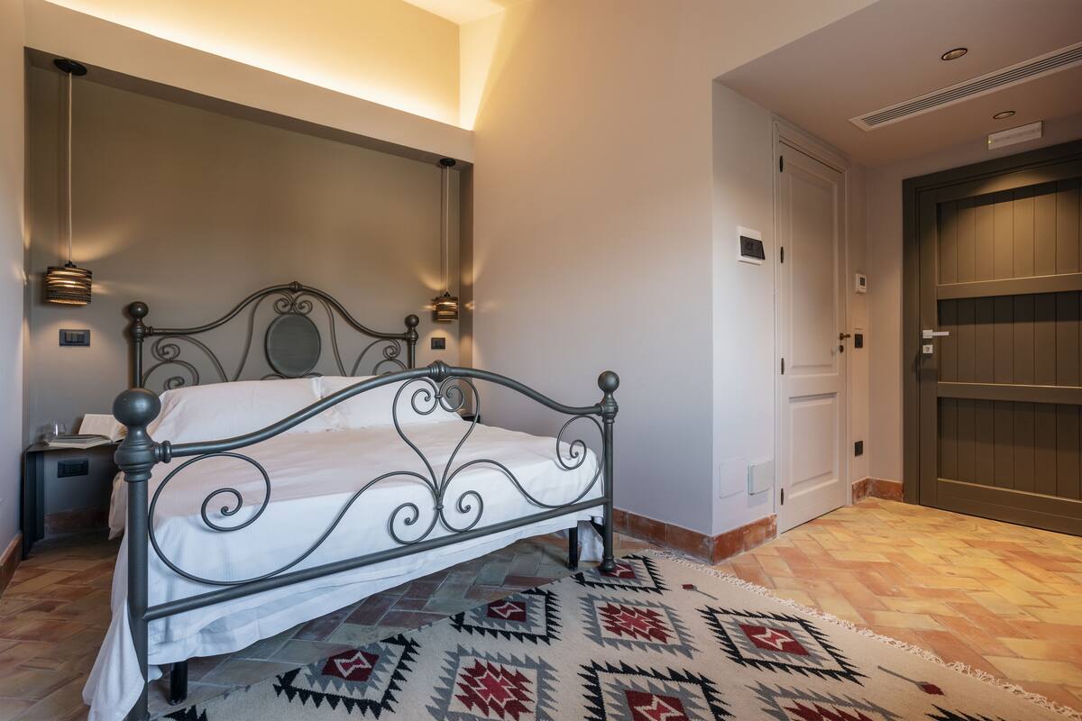 A neatly arranged bedroom with a metal bed frame, a patterned rug, and a nightstand with a lamp.