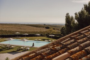 Un espace piscine agrémenté de chaises longues et de parasols, entouré d’un jardin aménagé et offrant une vue sur des collines lointaines.