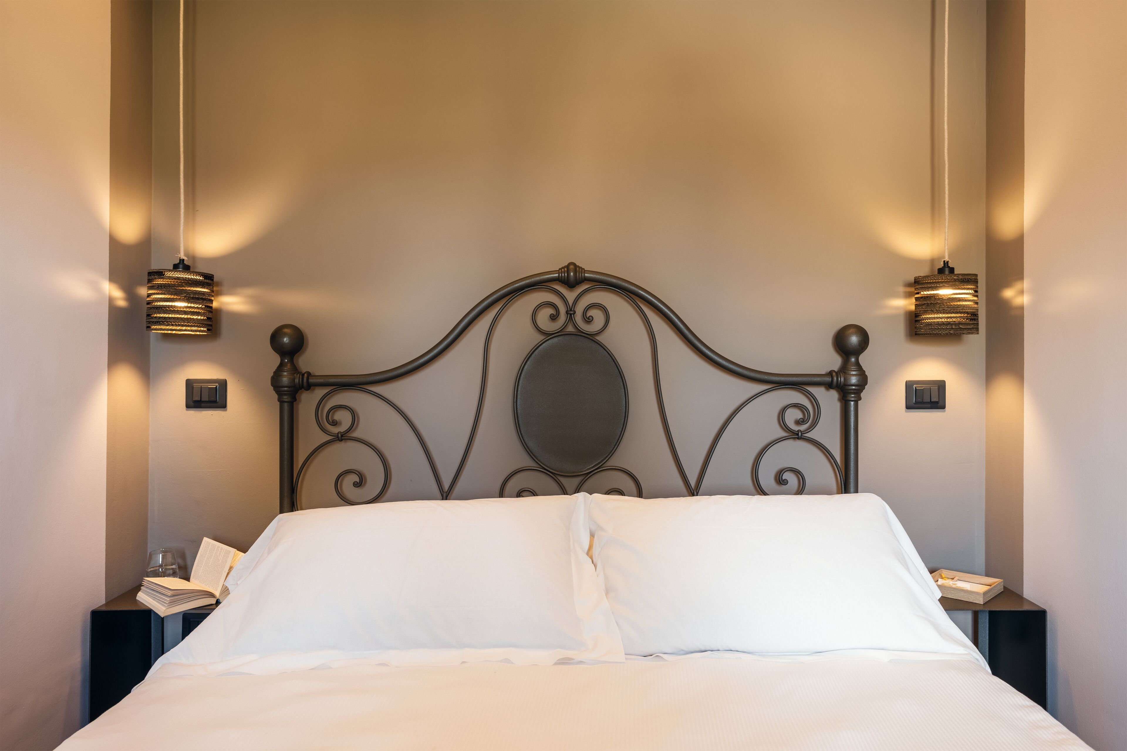 A neatly made bed with white linens, a metal headboard with decorative scrollwork, and two bedside lamps on matching nightstands.