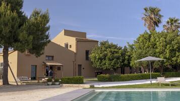 A modern building with a swimming pool, outdoor seating, and greenery.