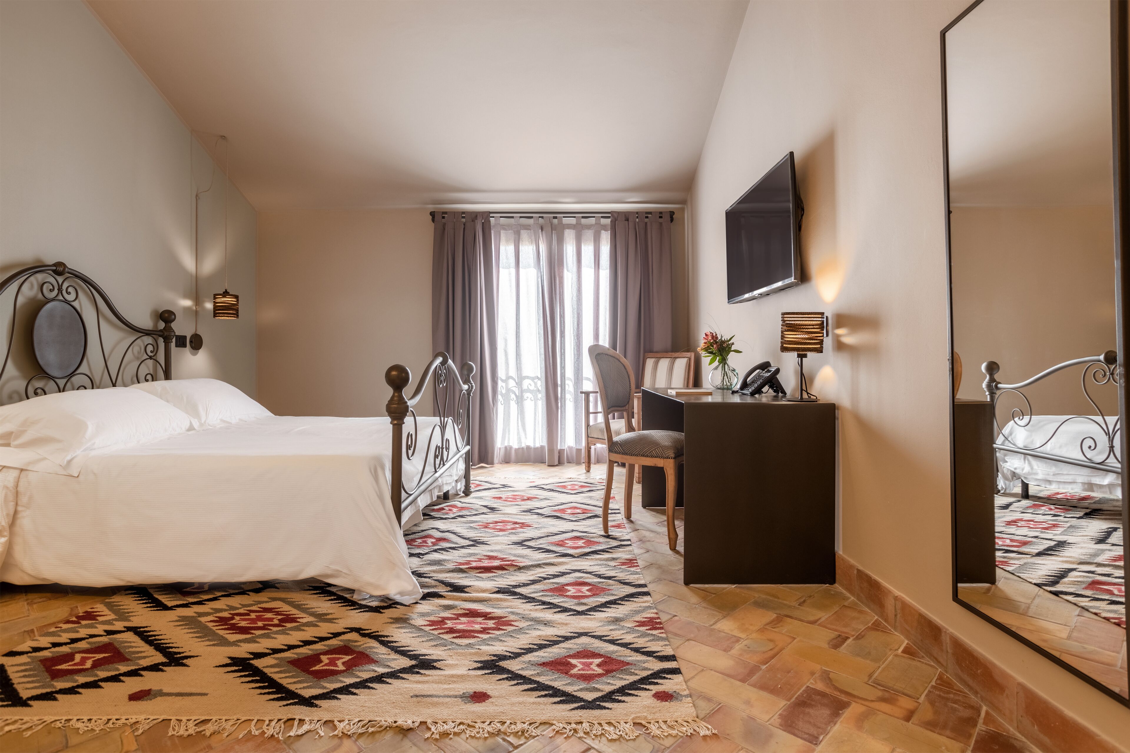 Een hotelkamer met een bed, een bureau, een stoel, een grote spiegel en een kamerkleed met een patroon.