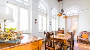 Un espace repas comprenant une table et des chaises en bois, un lustre et une vue sur l’extérieur grâce à de grandes fenêtres.