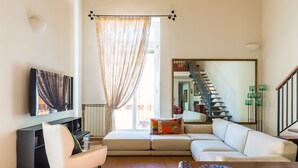Un salon comprenant un canapé, un fauteuil, un téléviseur, une table basse en bois et un tapis à motifs.