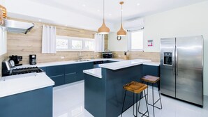 Een moderne keuken met een centraal eiland, roestvrijstalen apparatuur, hanglampen en uitzicht op de omgeving.