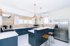 A modern kitchen with a central island, stainless steel appliances, pendant lighting, and a view of the outdoors. - Incredible 4BR with Private Pool near Eagle Beach (Noord)