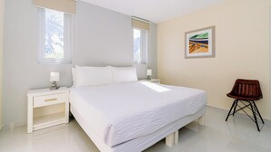 Une chambre d’hôtel avec un grand lit, deux tables de chevet, une chaise et un ventilateur de plafond.