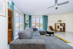 A modern living room with a grey sectional sofa, a small round table, a bookshelf, and a ceiling fan.