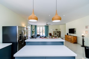 Una cocina moderna con una isla central, un comedor con sofá y un televisor en la sala.