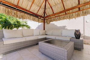A covered outdoor seating area with a wicker sofa and a coffee table.