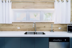 A kitchen with a stainless steel sink, a dishwasher, and a window with three framed pictures. - Incredible 4BR with Private Pool near Eagle Beach (Noord)