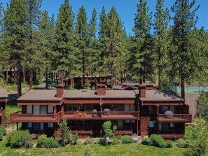 A multi-story lodge with a wooden exterior, multiple balconies, and a tennis court visible in the background.