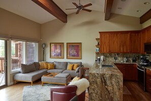 A spacious living room with a gray sectional sofa, a red armchair, and a marble kitchen island.