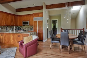 A spacious kitchen with wooden cabinets, a granite countertop, and modern appliances. There is a dining area with a wooden table and black chairs.