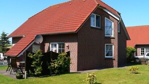 Une maison à deux étages, construite en briques, avec un toit recouvert de tuiles rouges, une antenne parabolique et un petit jardin comprenant une pelouse et quelques plantes.